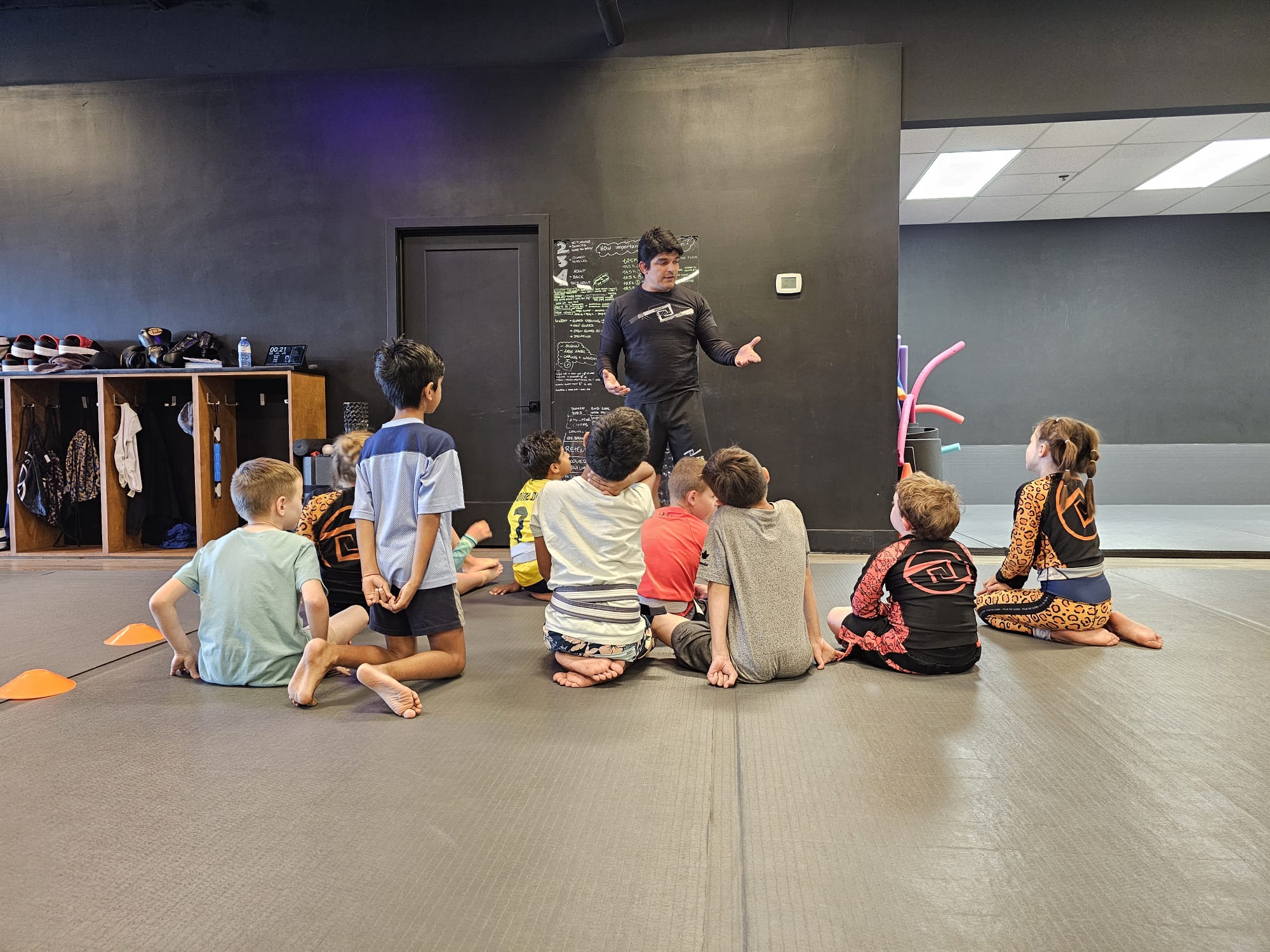 Coach teaching a group of kids sitting on the mats at Knots Jiu-Jitsu
