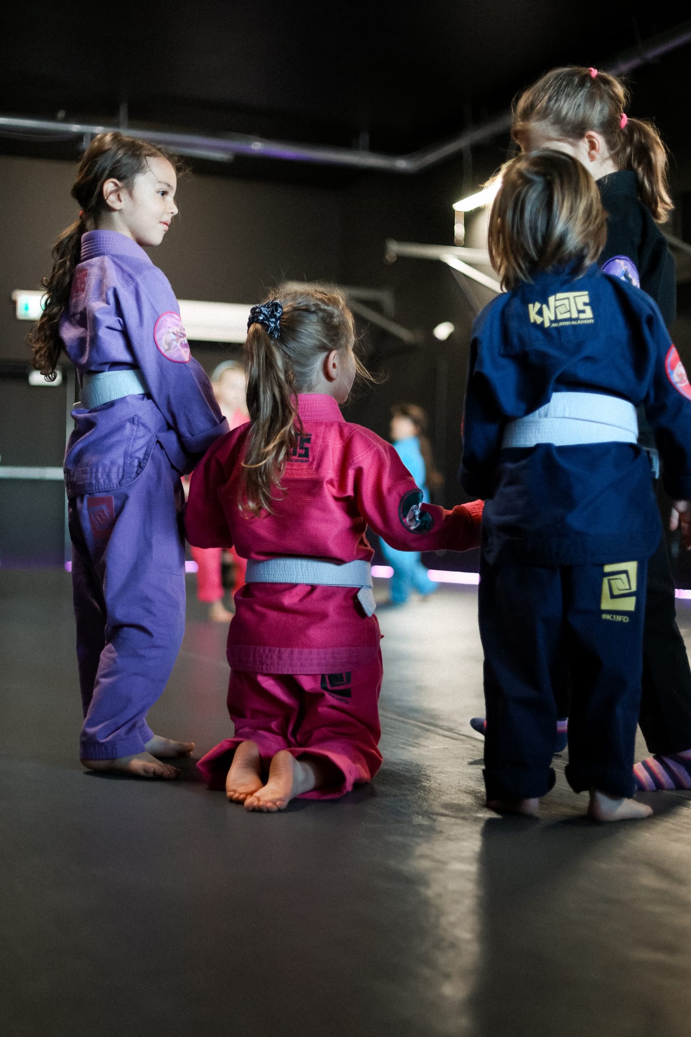 Three young girls in colorful Knots gis on the mats at Knots Jiu-Jitsu